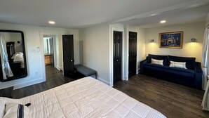 A bedroom with a large bed, a dark blue sofa, and a painting on the wall. - 112 S Washington Avenue (Lewes)