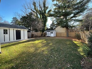 A backyard with a white shed, a wooden fence, and a large tree.