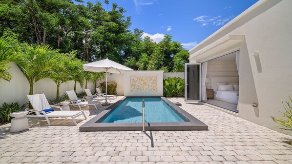 A swimming pool with lounge chairs and a covered area, surrounded by greenery. - Porters Place 18 4 Bedroom Villa (Holetown)