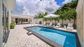 A swimming pool with a tiled deck, lounge chairs, and a covered patio area. - Porters Place 18 4 Bedroom Villa (Holetown)
