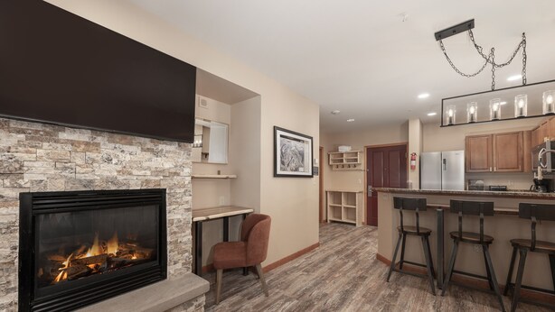A modern kitchen with a stone fireplace, wooden bar stools, and a bar area. - Premium Unit 2216 - One Bedroom - Zephyr Mountain Lodge 1 Condo (Winter Park)