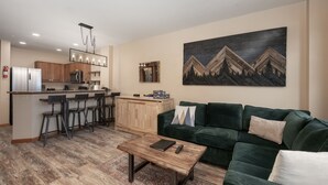 A modern living room with a green sofa, a coffee table, and a kitchen area with a bar and stools. - Premium Unit 2216 - One Bedroom - Zephyr Mountain Lodge 1 Condo (Winter Park)
