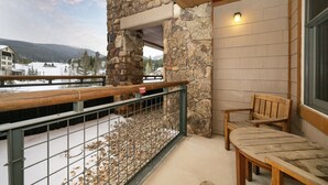 A balcony with a stone wall, a wooden bench, and a view of a snowy landscape. - Premium Unit 2216 - One Bedroom - Zephyr Mountain Lodge 1 Condo (Winter Park)