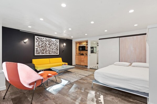 A modern hotel room with a bed, a yellow sofa, a red chair, a small table, and a kitchen area in the background. - Downtown Aspen Studio Steps to Gondola & Trails - 305A (Aspen)