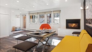 Ein modernes Wohnzimmer mit Kamin, einer Essecke mit Tisch und Stühlen sowie einem gelben Sofa.