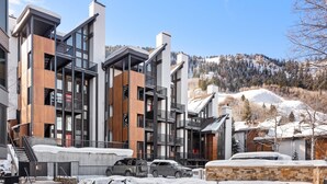 Ein modernes mehrgeschossiges Gebäude mit Balkonen, einer Steinfassade und Blick auf einen verschneiten Berg.