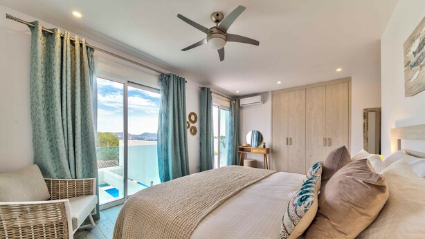 Ein Schlafzimmer mit einem großen Bett, einem Deckenventilator, Blick ins Freie und einem Balkon.