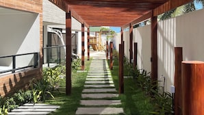 Un pasillo cubierto con techo de madera, paredes de ladrillo y un sendero de césped que conduce a un edificio.