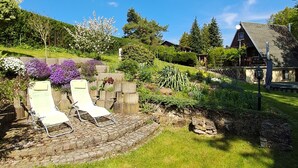 Un jardín con dos sillones de descanso, un muro de piedra y una cabaña de madera al fondo.