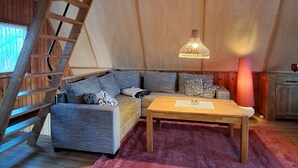 Un dormitorio tipo loft acogedor con una escalera de madera, un sofá, una mesa de centro de madera y una lámpara colgante.