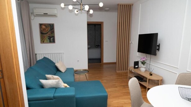 Una sala de estar moderna con un sofá color turquesa, una mesa de comedor redonda y un televisor montado en la pared.