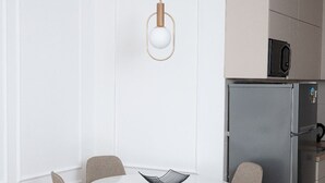 Una cocina moderna con una mesa de comedor blanca, cuatro sillas, una lámpara colgante y un refrigerador de acero inoxidable.