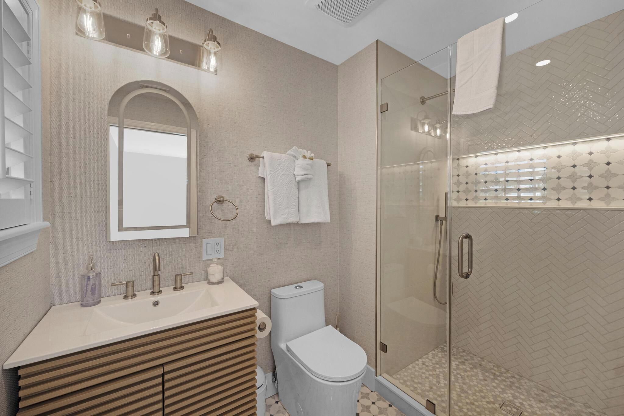A modern bathroom with a large mirror, a sink, a toilet, and a glass-enclosed shower.