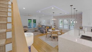 Un salon moderne avec un canapé, une table basse et un coin repas. On y trouve un escalier avec une rampe en bois et une vue sur l’extérieur.