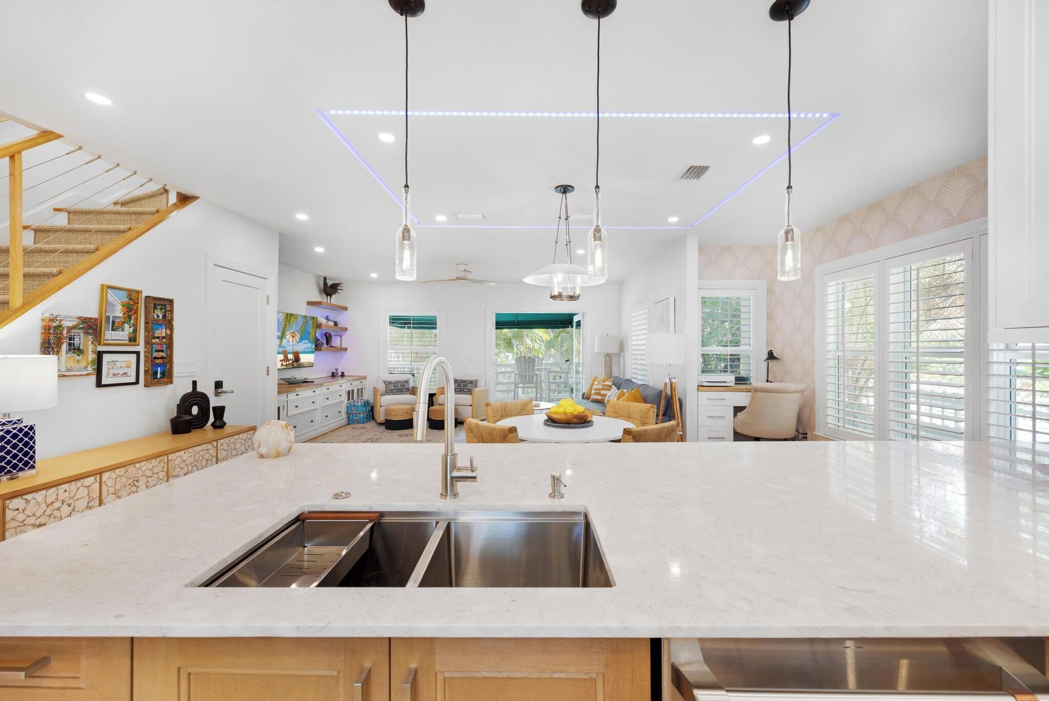 A modern kitchen with a central island, stainless steel appliances, pendant lighting, and a staircase with a wooden finish.