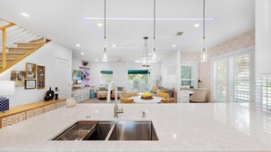 Une cuisine moderne dotée d’un îlot central, d’appareils électroménagers en acier inoxydable, de luminaires suspendus et d’un escalier avec des éléments en bois.
