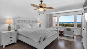A bedroom with a bed, nightstands, a ceiling fan, and a view of the ocean. - Gulf views & easy beach access + Free Tickets: Bikes, Dolphin Cruise & More! (Inlet Beach)