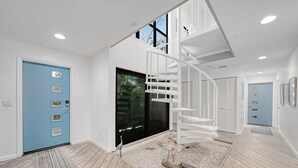 Un interior moderno con una escalera en espiral, una puerta azul y un ventanal grande.