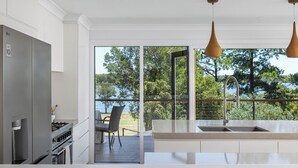 A modern kitchen with a large window, a built-in oven, and a dining area with a view of the outdoors. - Rivers Edge Oasis -Karuah, Infinity Pool and Private Cinema room (Karuah)