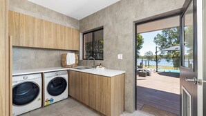 A compact kitchen with built-in appliances, a large window, and a view of an outdoor deck. - Rivers Edge Oasis -Karuah, Infinity Pool and Private Cinema room (Karuah)