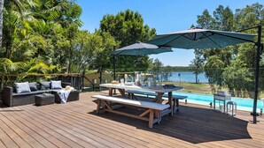A wooden deck with a picnic table, outdoor seating, and a view of a lake. - Rivers Edge Oasis -Karuah, Infinity Pool and Private Cinema room (Karuah)