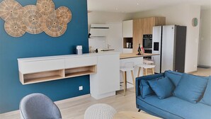 Un espace de vie moderne avec un mur d’accent bleu, un coin cuisine doté de meubles blancs, une table à manger et un canapé bleu.