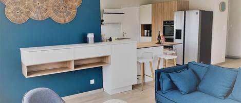 Un espacio habitable moderno con una pared de acento azul, una zona de cocina con armarios blancos, una mesa de comedor y un sofá azul.