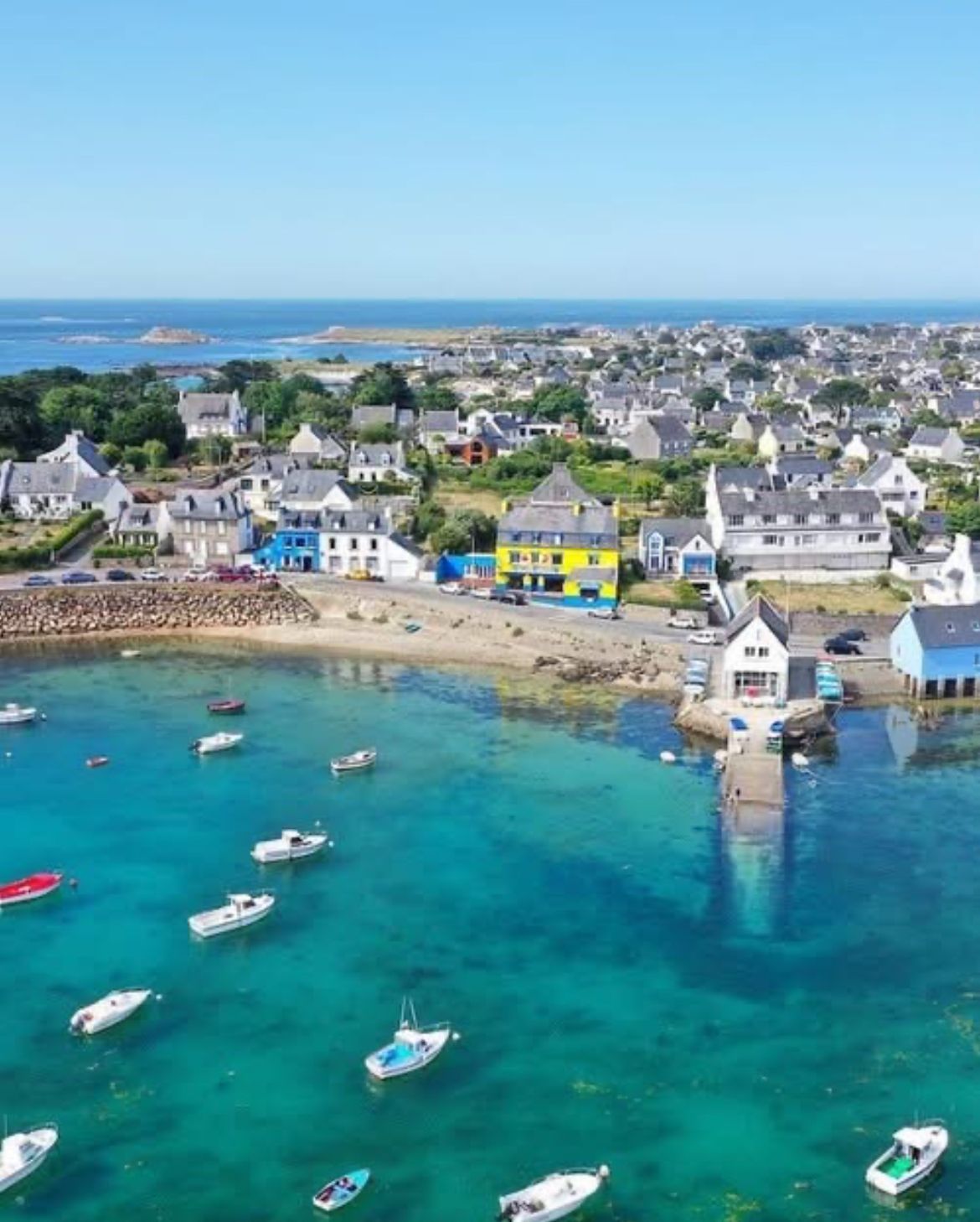 Un pueblo costero con casas coloridas, un puerto deportivo con barcos y una vista despejada del mar.