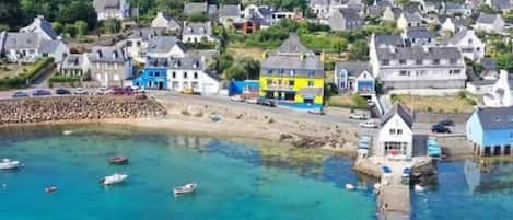Un pueblo costero con casas coloridas, un puerto deportivo con barcos y una vista despejada del mar.