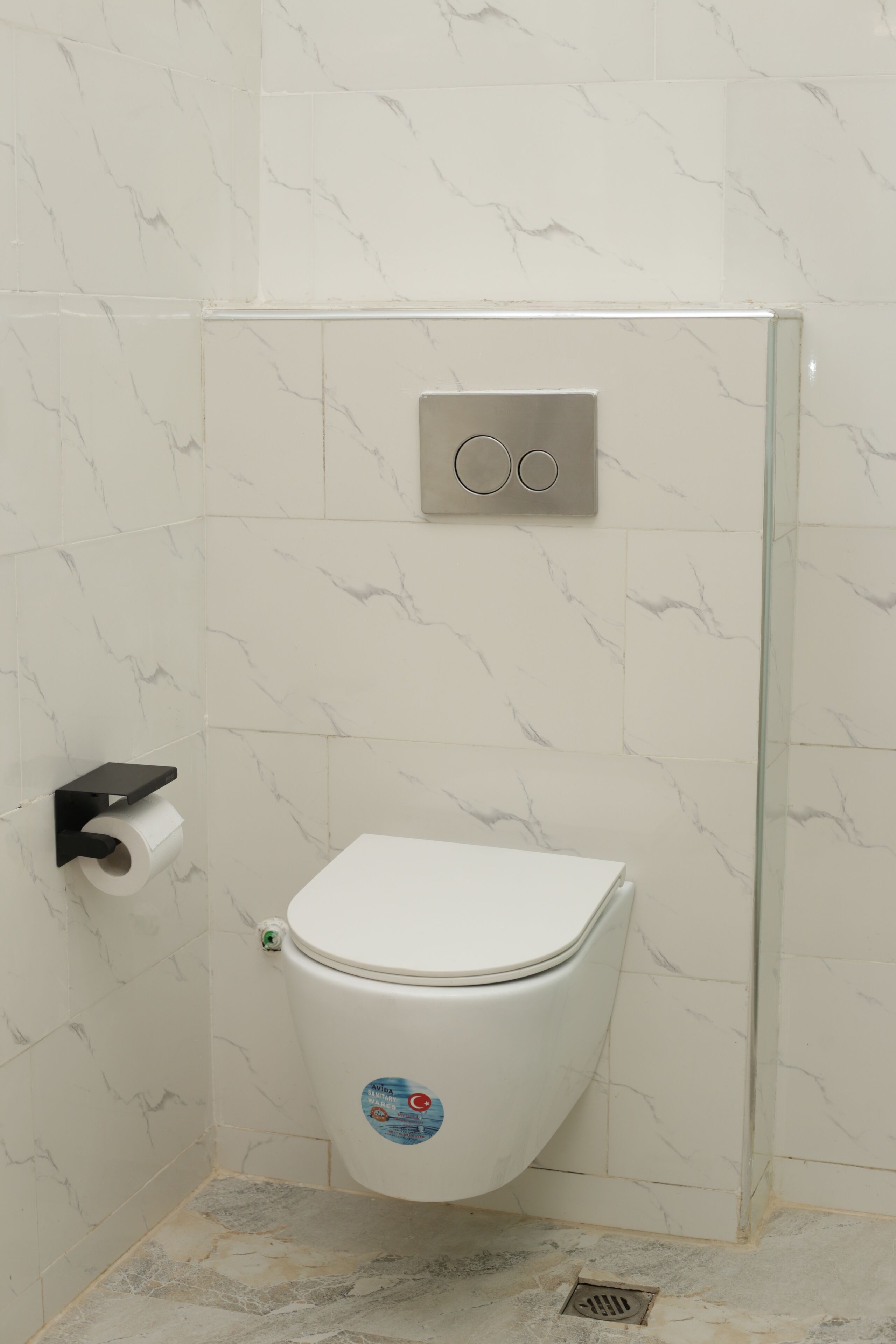 A bathroom with a white toilet, marble-patterned walls, and a glass shower enclosure.
