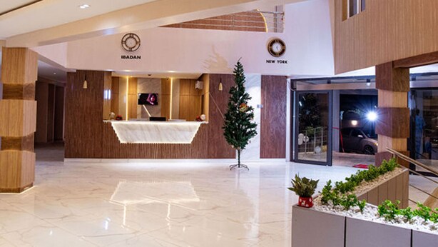 A modern hotel lobby with a reception desk, a Christmas tree, and a sign indicating 'New York' and 'IBADAN'. - The Bridge Hotel (Ibadan)