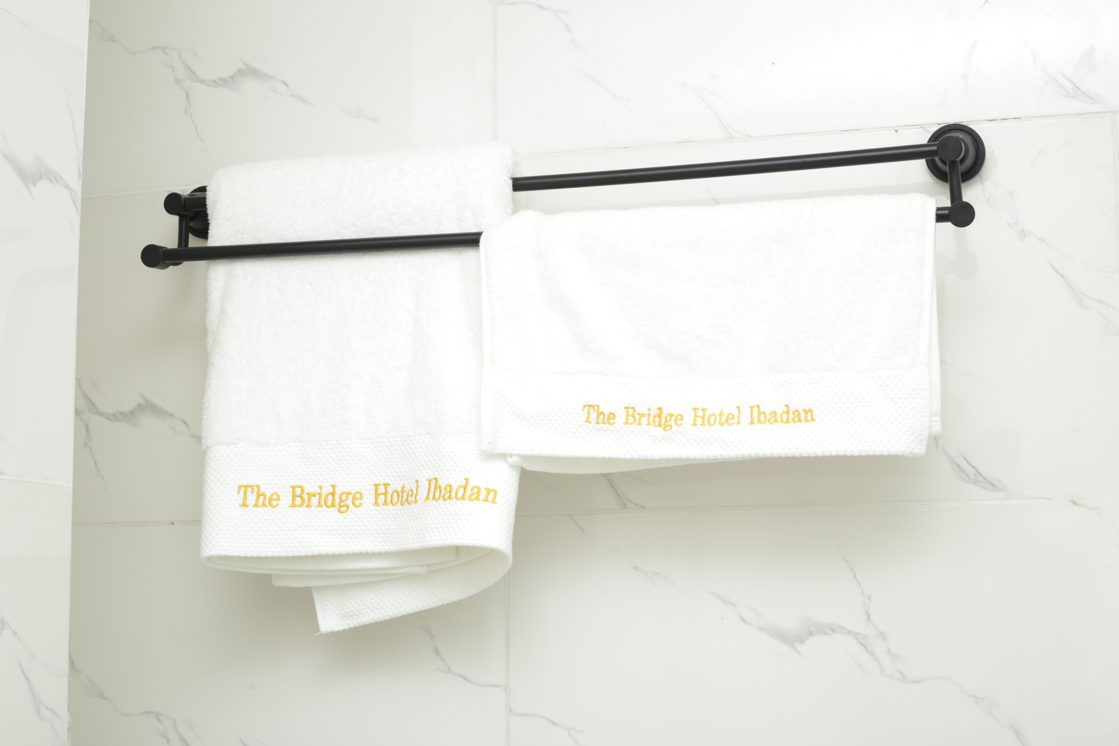 Two white towels hanging on a black towel rack with the text "The Bridge Hotel Ibadan" on them.