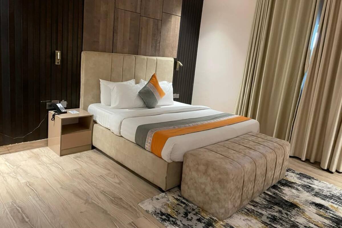A modern hotel room with a large bed, a bedside table with a phone, a small nightstand, and a large window with curtains.
