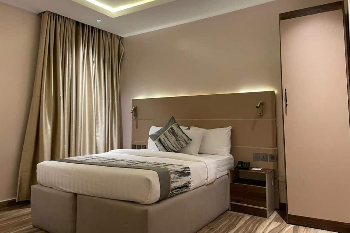 A hotel room with a large bed, a bedside table, a nightstand, and a door.