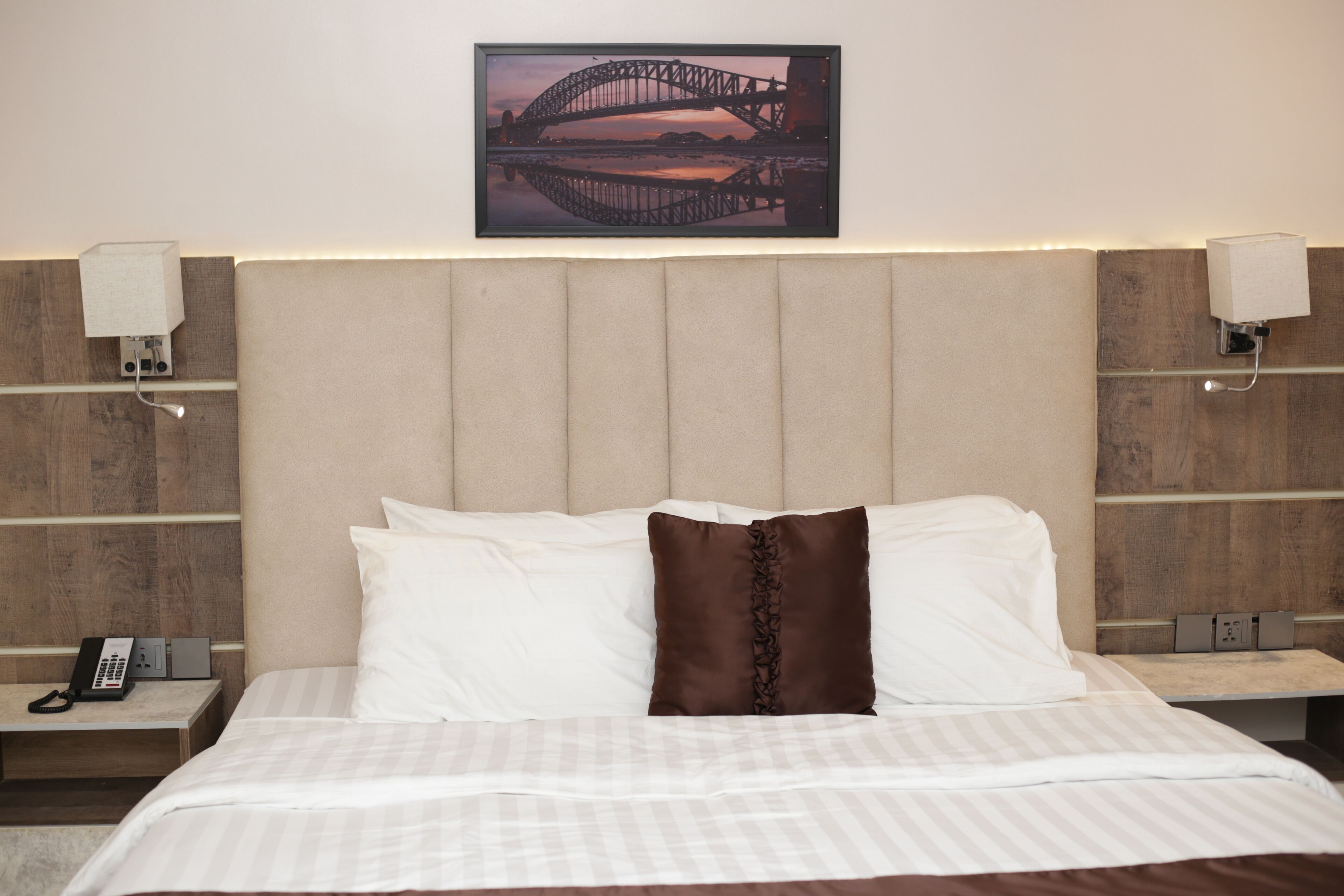 Une chambre d’hôtel avec un grand lit, une tête de lit, des lampes de chevet, un téléphone et un tableau encadré au mur.