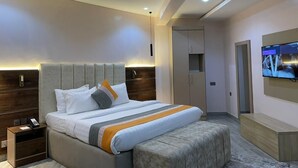 A modern bedroom with a large bed, a bedside table, a TV mounted on the wall, and a wardrobe. - The Bridge Hotel (Ibadan)