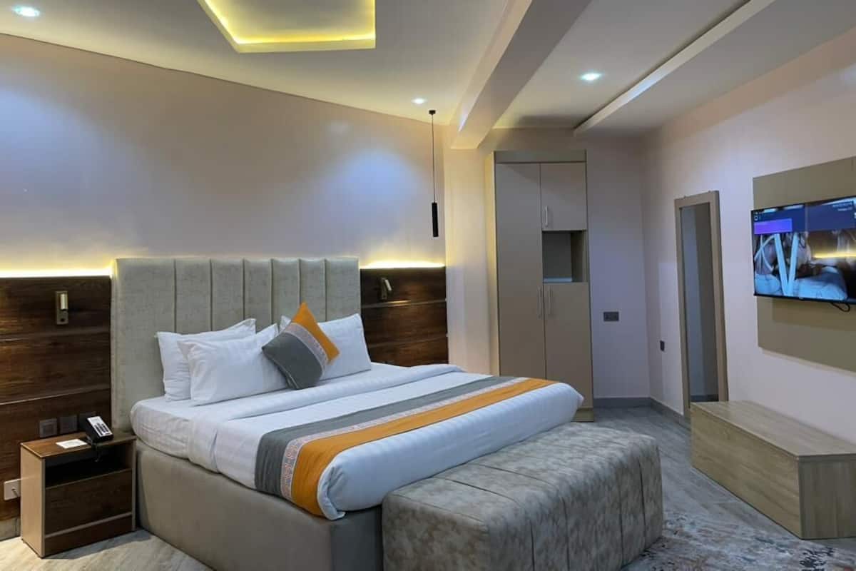 A modern bedroom with a large bed, a bedside table, a TV mounted on the wall, and a wardrobe.