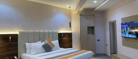 A modern bedroom with a large bed, a bedside table, a TV mounted on the wall, and a wardrobe.