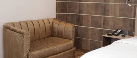 A hotel room with a brown sofa, a wooden headboard, a bedside table with a phone, and a white bed.