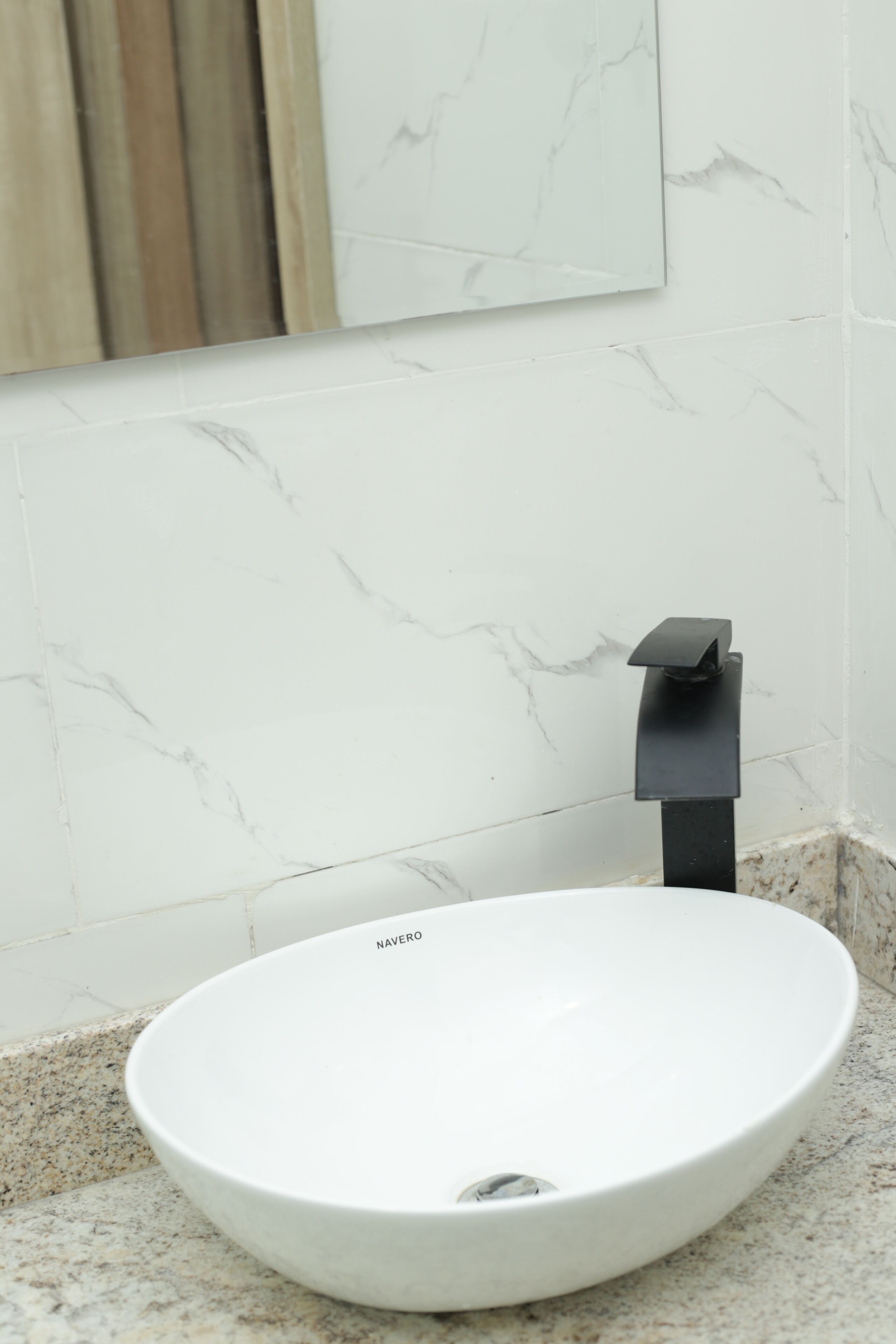 A white ceramic sink with a black faucet in a bathroom with marble walls and a granite countertop.