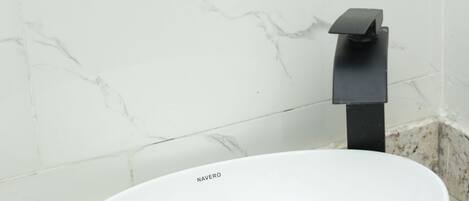 Un évier en céramique blanche, doté d’un robinet noir, dans une salle de bain aux murs en marbre et au comptoir en granit.