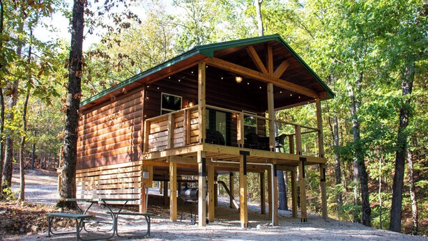 A wooden cabin with a balcony, surrounded by trees. - Cozy Treehouse For 2 | Outdoor Spa Tub + Fire Pit (Hot Springs)