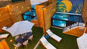 A modern outdoor pool area with wooden walls, a glass-enclosed pool, and a dining area with a table and chairs.