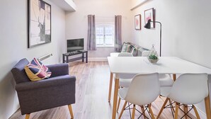 A modern living room with a grey sofa, a TV, a dining table with chairs, and a window with curtains. - Host & Stay | Roper Road (Canterbury)
