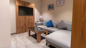 A modern living room with a grey sofa, a wooden accent wall, a flat-screen TV, and a coffee table. - RASIA HOTEL  (Jeddah)