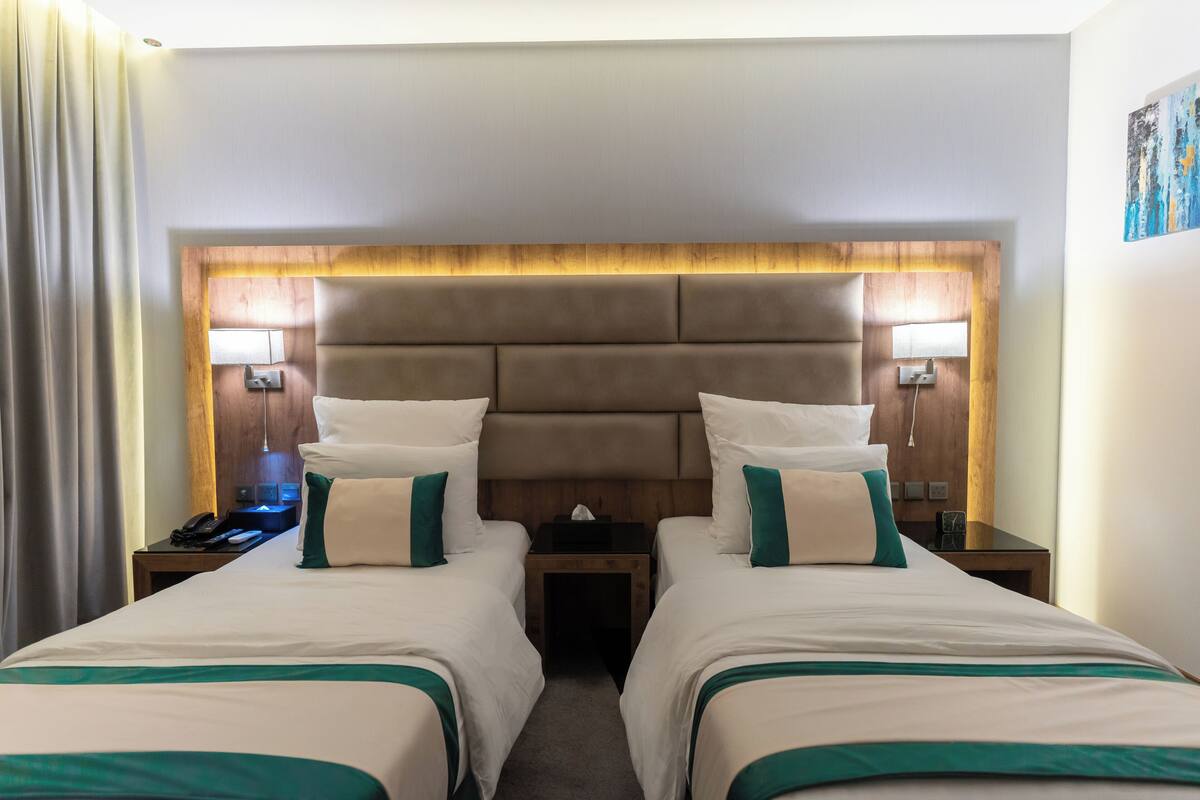 Quarto de hotel com duas camas, cabeceira de madeira, abajures e mesa de cabeceira com telefone.
