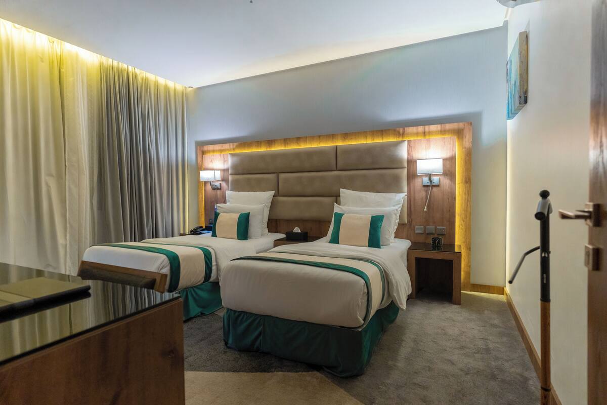 Quarto de hotel com duas camas, uma escrivaninha e uma mesa de cabeceira.