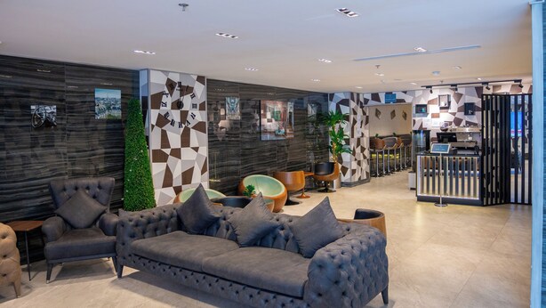 A modern hotel lobby with a grey sofa, armchairs, and a reception desk. - RASIA HOTEL  (Jeddah)