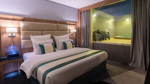 A hotel room with a large bed, bedside lamps, a wooden headboard, a view of a pool area, and a nightstand with a phone. - RASIA HOTEL  (Jeddah)