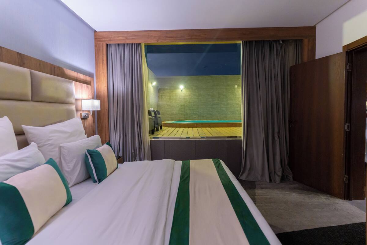 Quarto de hotel com uma cama grande, vista para uma piscina e cabeceira de madeira.